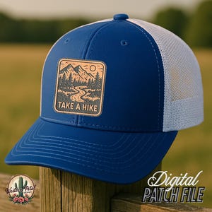 Puede incluir: Una gorra de camionero azul y blanca con un parche marrón que dice "Take a Hike" y una escena de montaña.