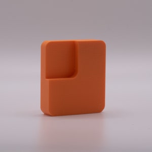 May include: An orange plastic shape with a cutout in the corner. The shape is a square with a smaller square cut out of the top right corner.