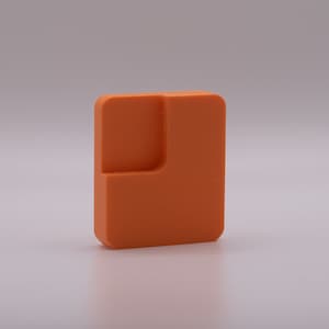 May include: An orange plastic puzzle piece with a unique shape. The piece has a smooth, textured surface.