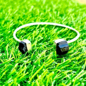 May include: A silver bangle bracelet with two black tourmaline stones on either end.