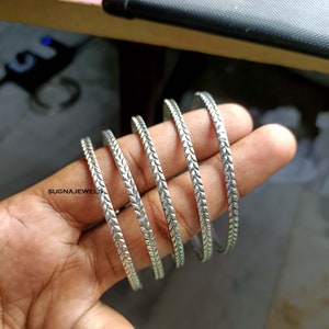 May include: Five silver bangles with a textured, leaf-like design. The bangles are stacked on top of each other.