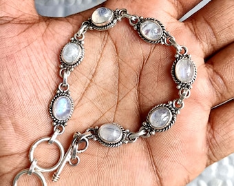 Op de afbeelding: Een zilveren armband met een schuifgesp heeft ovale maansteen edelstenen. De armband heeft een delicaat, ingewikkeld ontwerp.