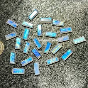 Könnte beinhalten: Eine Sammlung von 20 regenbogenfarbenen, rechteckigen Labradorit-Edelsteinen in Blau und Weiß. Die Steine liegen auf einer schwarzen Oberfläche.