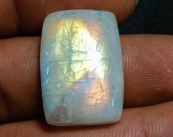 May include: A white, iridescent moonstone cabochon with a rectangular shape. The stone has a rainbow sheen and is set in a silver ring.