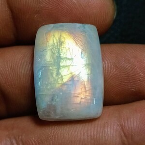 May include: A white, iridescent moonstone cabochon with a rectangular shape. The stone has a rainbow sheen and is set in a silver ring.