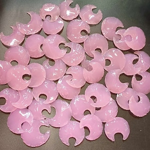 Puede incluir: Una colección de piezas de vidrio de color rosa en forma de media luna. Las piezas son translúcidas y tienen un acabado liso y pulido.