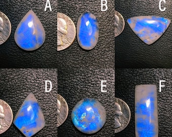 May include: Six different moonstone cabochons in various shapes and sizes, including teardrop, oval, and rectangular. The stones are all a milky white color with a blue iridescent sheen.