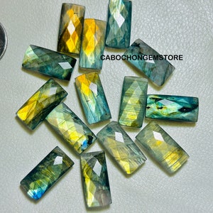 May include: A collection of rectangular labradorite gemstones with faceted surfaces. The stones display a mix of colors, including blues, greens, and yellows. The text "CABOCHONGEMSTORE" is visible on the image.
