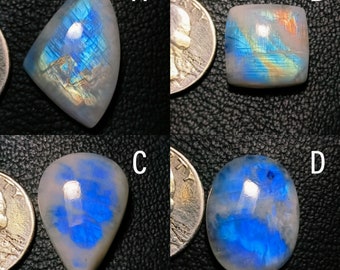 May include: Four iridescent moonstone cabochons in various shapes and sizes, including a teardrop, oval, square, and triangular shape. The stones are all a milky white color with blue and green iridescent flashes.