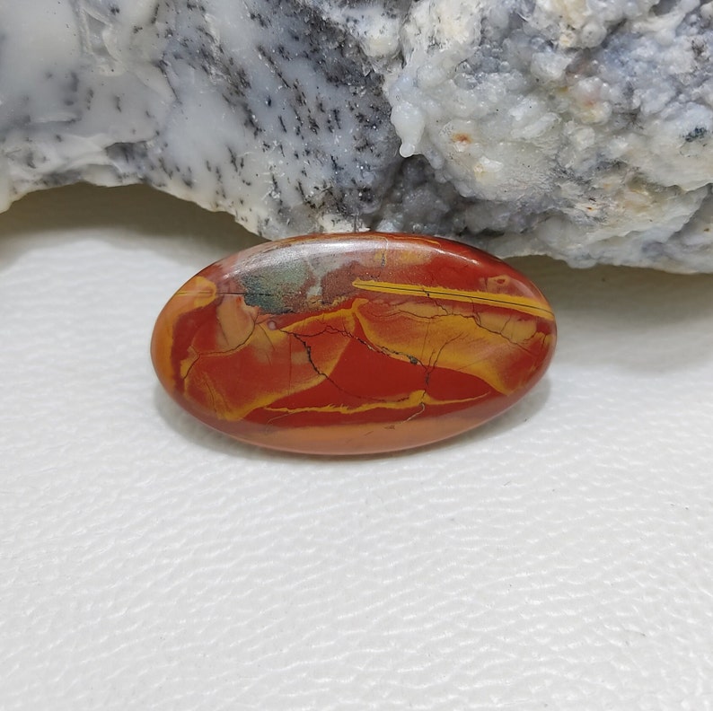 Puede incluir: Una piedra preciosa ovalada en cabuj&oacute;n con un patr&oacute;n de remolino en tonos rojos, amarillos y marrones.