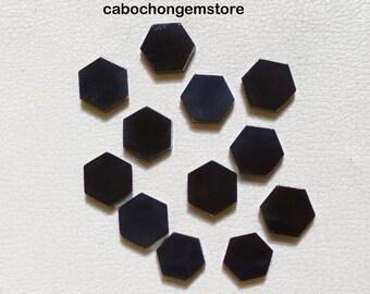 Può includere: Dodici cabochon esagonali neri, ognuno con una superficie liscia e lucida. I cabochon sono disposti in un motivo sciolto e disperso su uno sfondo bianco.