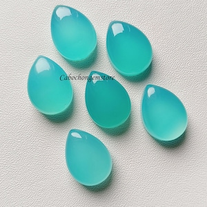 May include: Six teal blue teardrop-shaped cabochon gemstones on a white surface.  Cabochongemstore.
