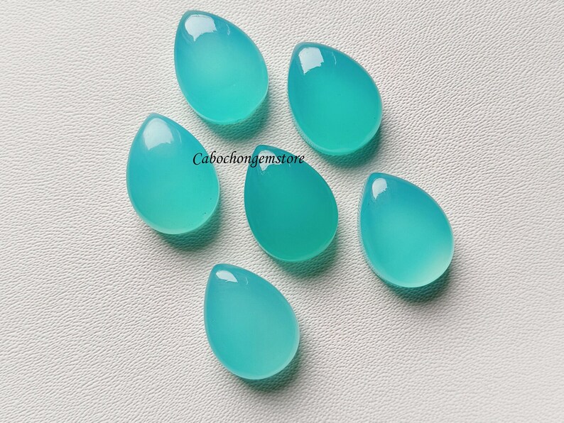 May include: Six teal blue teardrop-shaped cabochon gemstones on a white surface.  Cabochongemstore.