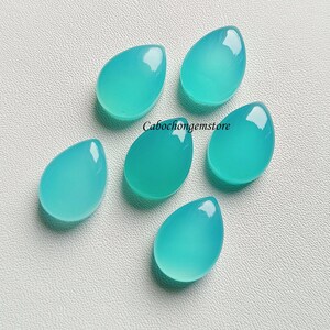 May include: Six teal blue teardrop shaped cabochon gemstones on a white background.