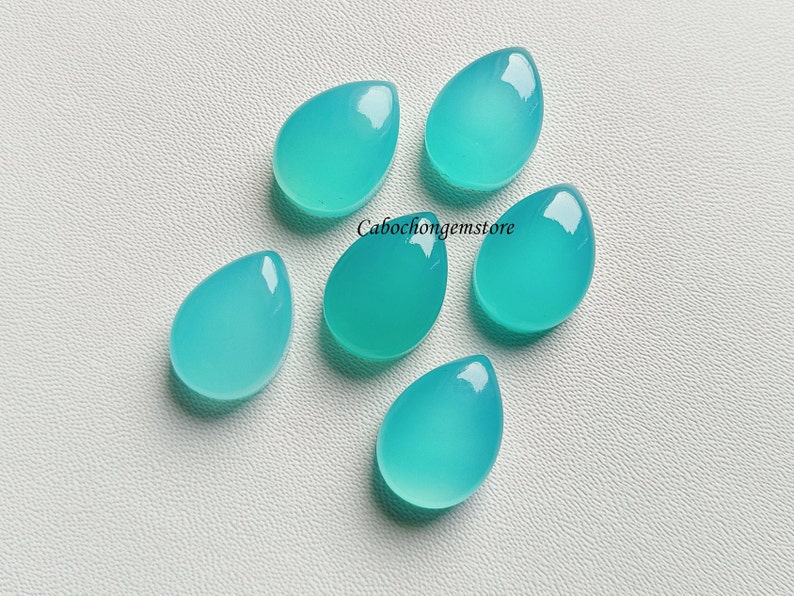 May include: Six teal blue teardrop shaped cabochon gemstones on a white background.