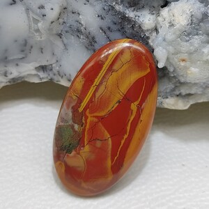 Puede incluir: Una piedra preciosa ovalada en cabuj&oacute;n con un acabado pulido. La piedra es roja, amarilla y marr&oacute;n con un patr&oacute;n de colores y vetas en espiral.