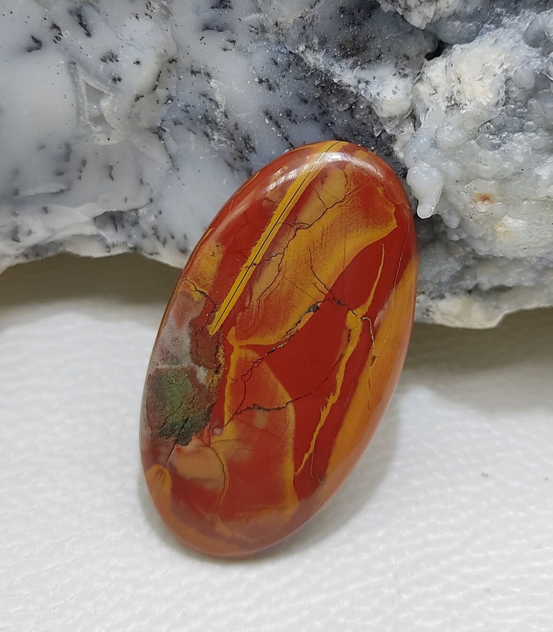 Puede incluir: Una piedra preciosa ovalada en cabuj&oacute;n con un acabado pulido. La piedra es roja, amarilla y marr&oacute;n con un patr&oacute;n de colores y vetas en espiral.