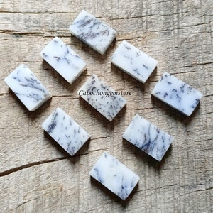 May include: Eight rectangular pieces of dendritic opal, each with a white base and black dendritic patterns. The stones are arranged on a wooden surface.