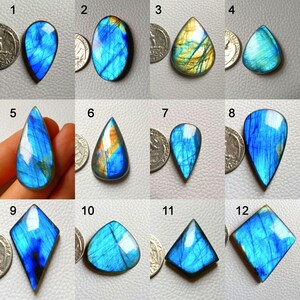 May include: A collection of twelve polished labradorite gemstones in various shapes, including teardrop, oval, and diamond. The stones display iridescent blue, gold, and green flashes. Each stone is shown next to a quarter for size comparison.