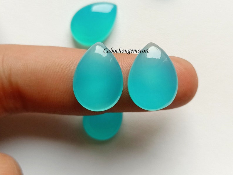 May include: Two teardrop-shaped turquoise cabochons, approximately 1 inch in length, are held between two fingers. The cabochons are smooth and polished.