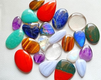 May include: A collection of polished gemstones in various shapes and colors, including red, blue, green, and purple. The gemstones are displayed on a white surface, showcasing their unique textures and patterns. A variety of shapes are present, including oval, teardrop, and irregular forms.