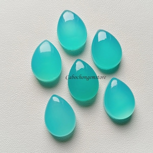 May include: Six teal blue teardrop shaped cabochon gemstones on a white surface.