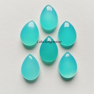 May include: Six teal blue teardrop shaped cabochons, each with a smooth, polished surface.  Cabochongemstore is printed in white text on the white background.
