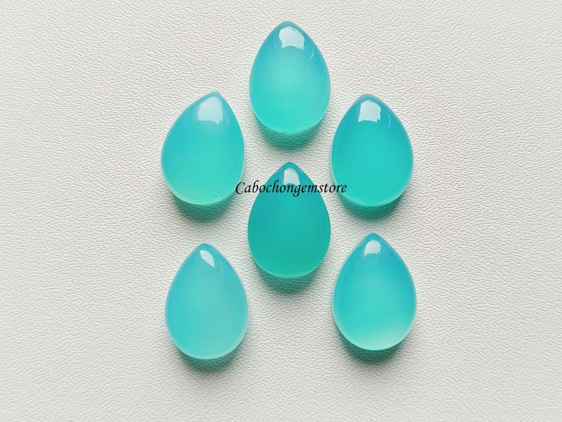 May include: Six teal blue teardrop shaped cabochons, each with a smooth, polished surface.  Cabochongemstore is printed in white text on the white background.