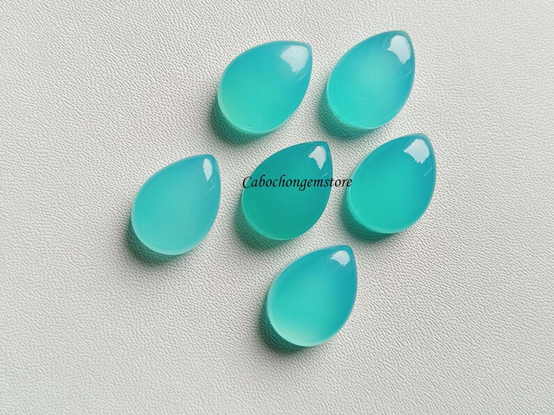 May include: Six teardrop-shaped cabochons in a light turquoise color. The stones are smooth and polished, and they are arranged in a cluster on a white surface.