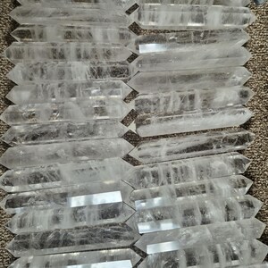 May include: A collection of clear quartz double-terminated points, also known as double-ended crystals. The points are arranged in rows, showcasing their natural crystal formations.