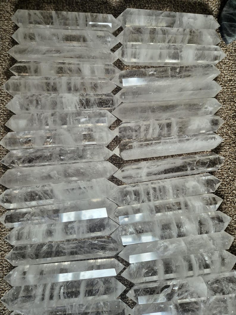 May include: A collection of clear quartz double-terminated points, also known as double-ended crystals. The points are arranged in rows, showcasing their natural crystal formations.