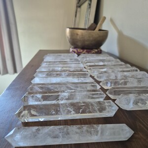 May include: A collection of clear quartz crystal points arranged in rows on a wooden surface. The points are all approximately the same size and shape, and they are all pointed at one end.