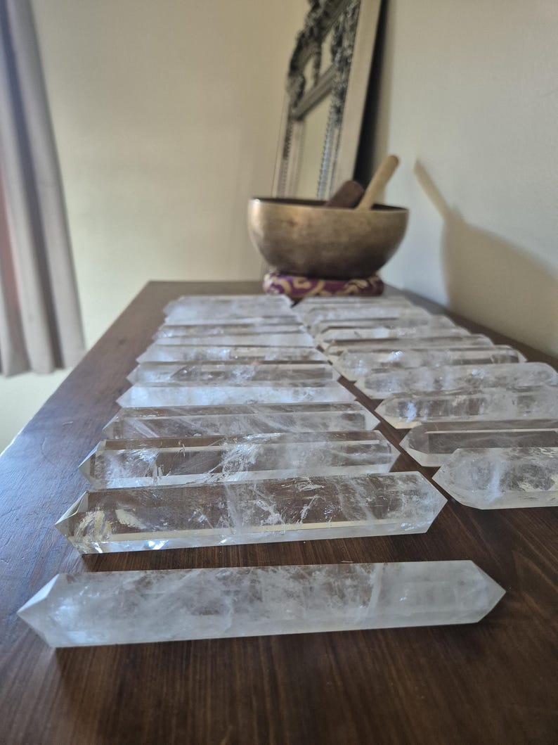 May include: A collection of clear quartz crystal points arranged in rows on a wooden surface. The points are all approximately the same size and shape, and they are all pointed at one end.