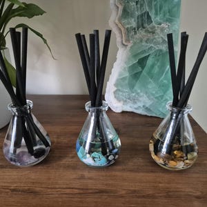 Può includere: Tre bottiglie diffusori in vetro con canne nere e pietre colorate all'interno. Le bottiglie sono trasparenti e hanno una finitura perlescente. Le pietre sono di diversi colori, tra cui blu, verde e marrone.