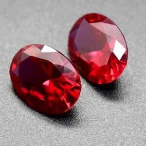 May include: Two oval-shaped, deep red gemstones with a faceted cut.