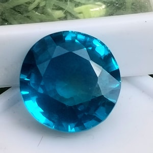 Può includere: Una gemma blu brillante con taglio sfaccettato. La gemma è rotonda e ha un'alta lucidatura.