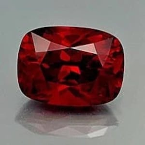 May include: A deep red gemstone with a cushion cut and many facets.
