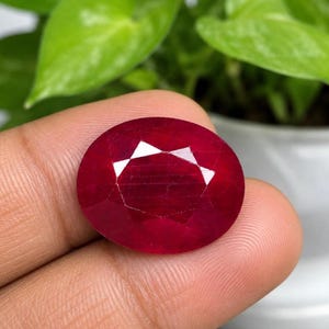 Könnte beinhalten: Ein tiefroter, oval geformter Edelstein mit facettierter Oberfläche. Der Stein zeigt einen satten, kräftigen Karmesinton und ein poliertes Finish, das das Licht über seine zahlreichen Schliffebenen reflektiert und klar und lebendig wirkt.
