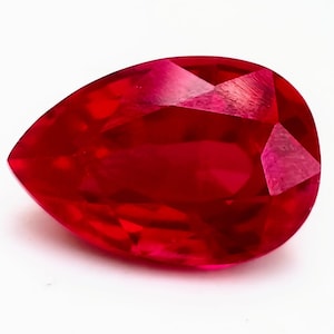 Puede incluir: Una piedra preciosa de rubí en forma de pera con un color rojo intenso. La piedra preciosa está facetada y tiene un alto pulido.