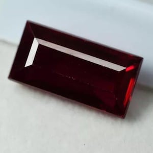 Könnte beinhalten: Ein rechteckiger, tief roter Edelstein mit Facettenschliff.