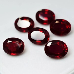 May include: Six oval-shaped, deep red gemstones. The gemstones are faceted and have a high polish.