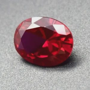 May include: A deep red oval-shaped gemstone with facets.