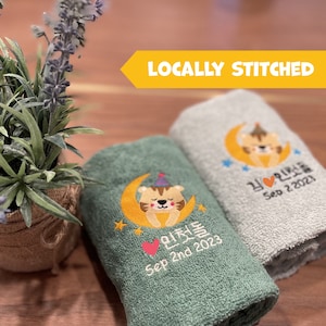 May include: Two green and gray towels with embroidered cartoon tigers wearing party hats on a crescent moon. The towels have Korean text and the dates "Sep 2nd 2023" and "Sep 2 2021".