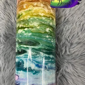 May include: A stainless steel tumbler with a colorful abstract design featuring shades of pink, orange, yellow, green, blue, and purple. The tumbler has a black lid and base. The text "Rainbow Moonlight Designs" is visible on the tumbler.