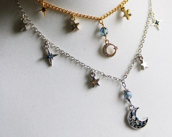 Puede incluir: Dos collares en capas con cadenas plateadas y doradas. Ambos collares presentan pequeños dijes de estrellas y un dije de media luna con acentos de cristal azul.