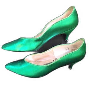 Könnte beinhalten: Ein Paar smaragdgrüne Satin-Pumps mit spitzer Zehenpartie und niedrigem Pfennigabsatz. Das Innere der Schuhe ist mit beigefarbenem Material ausgekleidet, wobei die Größe 8 B und weitere Produktcodes deutlich auf der Innenferse aufgedruckt sind.