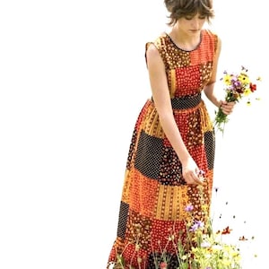May include: A sleeveless patchwork maxi dress in shades of orange, red, and brown. The dress features a black belt and a floral pattern. A person is holding a bouquet of wildflowers and picking flowers from a small patch of flowers.