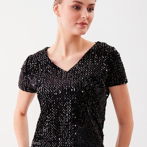 Puede incluir: Top negro con cuello en V y lentejuelas, con mangas cortas, combinado con una falda negra. La falda tiene cierre de botones y un dobladillo asimétrico. Ideal para una salida nocturna o un evento especial.