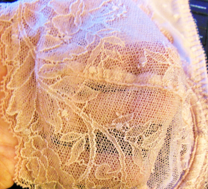 May include: Close-up of delicate, beige lace fabric with a floral pattern. The lace has a soft, airy texture and a subtle sheen.