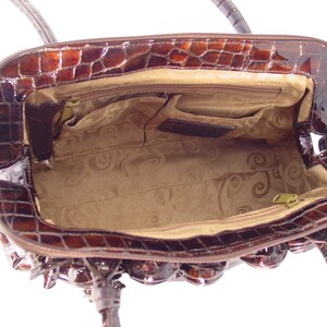 Pu&ograve; includere: Una borsa a mano satchel marrone in pelle con stampa coccodrilo con chiusura a zip superiore e un interno in tessuto marrone. La borsa a mano ha un manico superiore e una tracolla rimovibile.